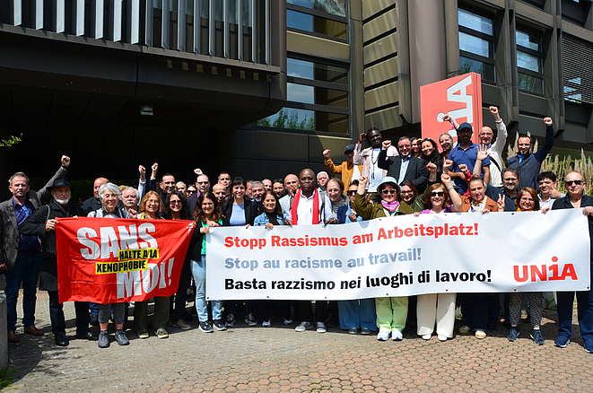 Des délégué-e-s de la conférence des migrations d'Unia derrière une banderole sur laquelle est écrit "Stop au racisme au travail!"