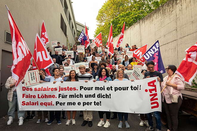 Teilnehmende der Fachgruppe Coop posieren vor einem Gebäude mit Transparenten und Unia-Fahnen: "Faire Löhne.Für mich und dich!"