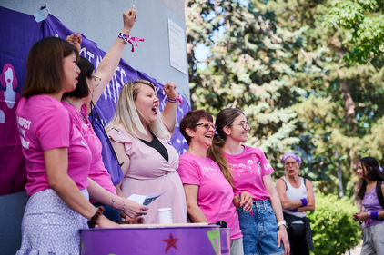 Cinque donne allegre e speranzose, con magliette rosa dello sciopero femminile e pugni alzati.