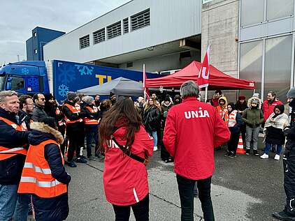 Versammlung von Streikenden und Gewerkschafter neben rotem Zelt vor einer Fabrik in der Schweiz