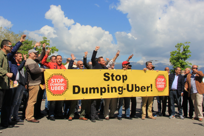 Des chauffeurs de taxis avec une banderole sur laquelle il est inscrit "Stop Dumping-Uber"