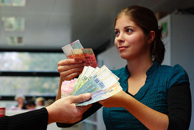 Junge Frau zeigt - mit Geldscheinen - einer Hand, ebenfalls mit Noten, das Ergebnis ihrer Lohnanalyse
