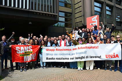 Des délégué-e-s de la conférence des migrations d'Unia derrière une banderole sur laquelle est écrit "Stop au racisme au travail!"