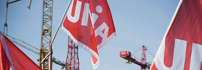Die Unia fordert einer Verstärkung der flankierenden Massnahmen (FlaM). Bild mit Unia-Fahne auf Baustelle.