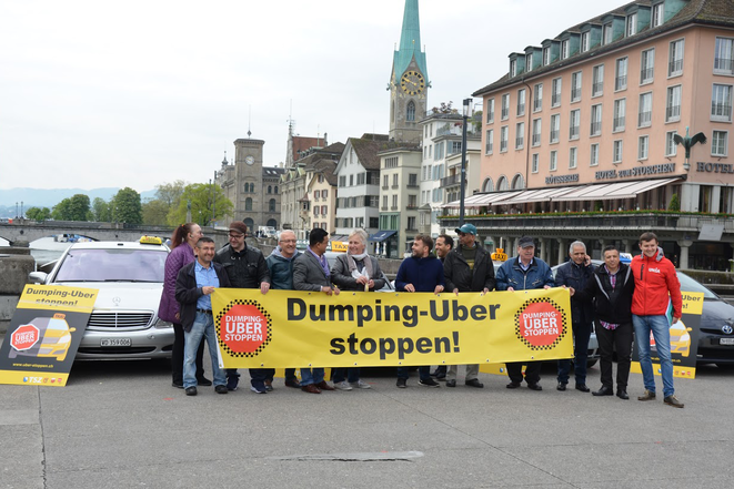 Des chauffeurs de taxi et des militant-e-s d'Unia se tiennent derrière une banderole critiquant Uber.