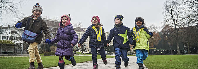 Fünf Kinder rennen lachend auf ihrem Weg in den Kindergarten.