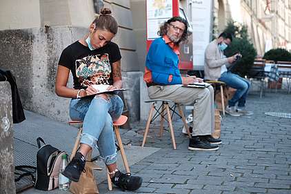 Una giovane donna si siede su uno sgabello nella città vecchia di Berna e scrive cartoline