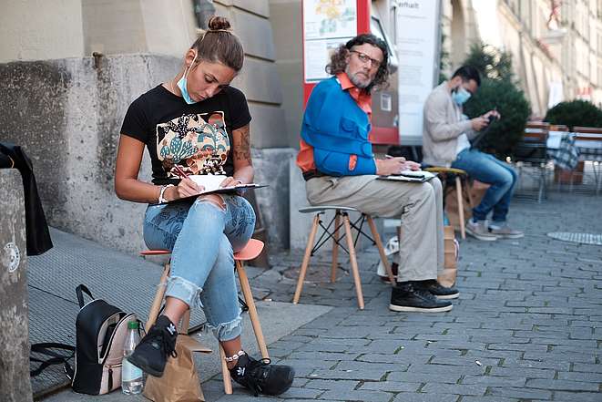 Una giovane donna si siede su uno sgabello nella città vecchia di Berna e scrive cartoline