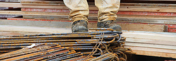Gros plan sur les chaussures d'un travailleur de la construction se tenant sur un tas de tiges d'armature en métal rouillées