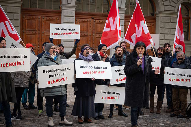 Vania Alleva, Präsidentin der Unia, am Mikrofon vor einer Gruppe Aktivist:innen mit Schildern wie: Über 6o Jahre alt: aussortiert 