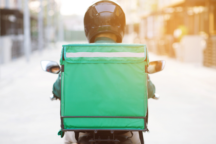 Essenslieferant bei der Arbeit, auf einem Motorrad fahrend, mit grüner Kiste am Rücken