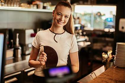 Eine junge Kellnerin lächelt hinter einer Theke.