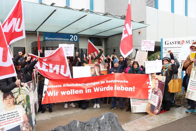 Des délégué-e-s d'Unia devant les bureaux de la faîtière GastroSuisse, avec une pancarte