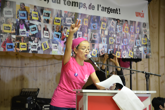 Junge Frau in rosa Frauen*streik-T-Shirt spricht mit erhobener Hand am Mikrofon