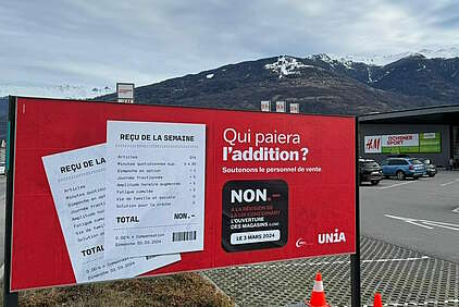 Rotes Plakat mit weissem Kaufbeleg auf Französisch vor einem Einkaufszentrum im Wallis