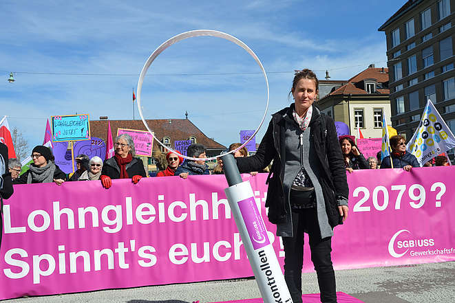 Demonstrierende  Frauen mit einer grossen Lupe auf dem Waisenhausplatz in Bern