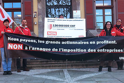 Militants d'Unia à Sion avec panneau: «(Drapeau valaisan)136'000'000 – Encore des cadeaux pour les gros actionnaires? ça suffit!»