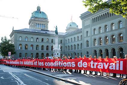 Des gens tracent la ligne rouge devant le Palais fédéral avec une banderole