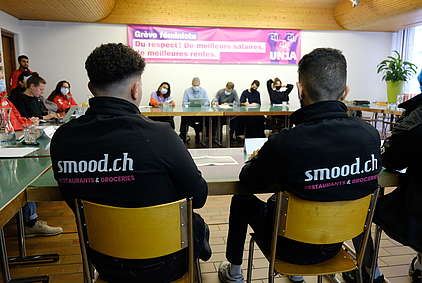 Deux employés de Smood assis de dos à la conférence de presse d'Unia sur leurs situation de travail précaires