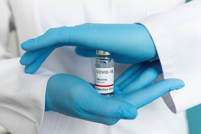 Des mains dans des gants en caoutchouc bleu tiennent une dose de vaccin contre le Covid-19