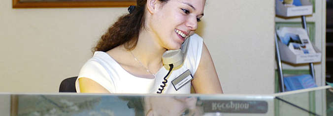 Frau im weisser Schürze und Namensschild hinter einer Reception am Telefon