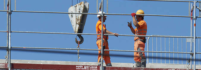 2 Bauarbeiter auf einem Dach vor blauem Himmel