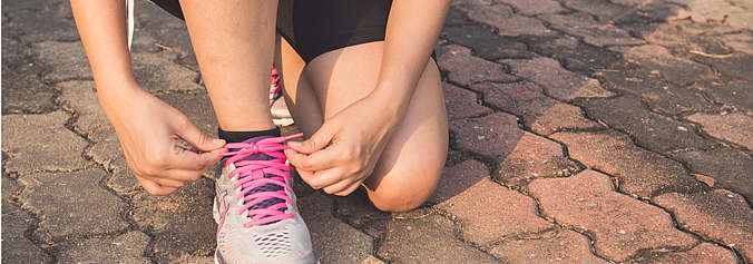 Una donna inginocchiata si allaccia una scarpa da ginnastica.