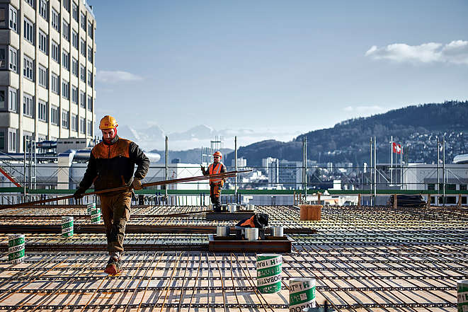 Zwei Bauarbeiter auf einer Baustelle vor Alpenpanorama