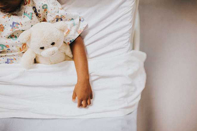 Arm eines Kindes mit Teddybär im Bett