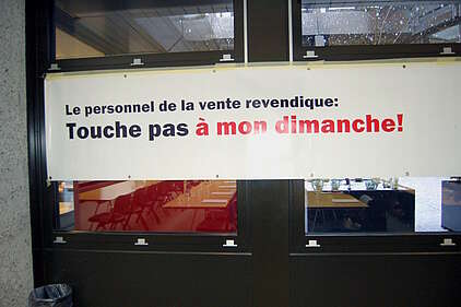 Banderole affichée contre des fenêtres avec le texte "Le personnel de vente revendique: Touche pas à mon dimanche!"