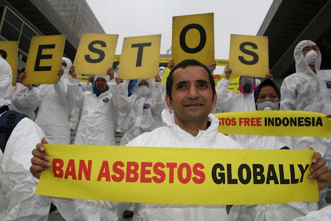 Demonstrant/innen mit englischen Transparenten fordern ein weltweites Verbot von Asbest. 